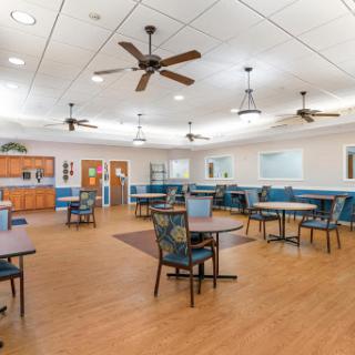 A spacious and well-lit dining area featuring tables and chairs, with ceiling fans for comfort.