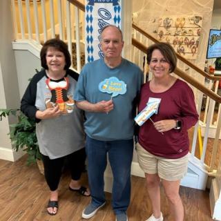 Three people standing indoors near a staircase, smiling and holding items.
