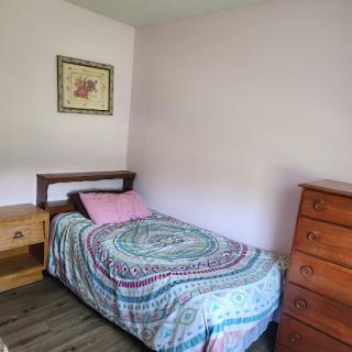 A cozy and simple bedroom featuring a single bed with a decorative blanket and a wooden nightstand.