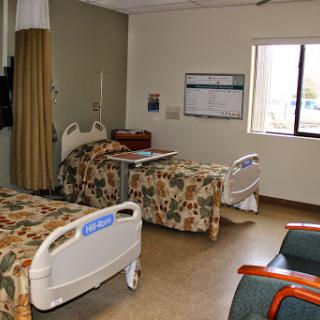 A view of a hospital patient room with two beds and natural light coming from the window.