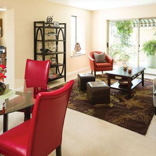 A modern living room with red chairs and a coffee table, featuring ample natural light.