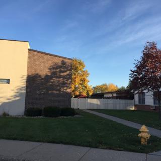 A view of a residential or commercial building with autumn trees in the foreground under a clear blue sky.