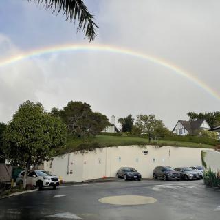 A beautiful rainbow arches over a parking lot on a cloudy day.