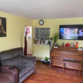 A cozy living room featuring a sofa, television, and piano with wooden flooring.