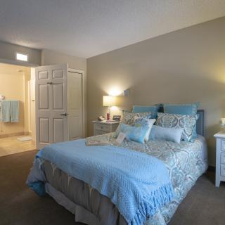 A cozy bedroom with a neatly made bed in light blue tones and soft lighting.
