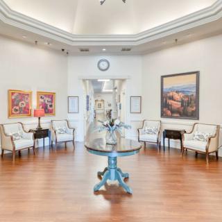 A well-lit lobby or waiting area with chairs arranged along the walls, featuring a central table and decorative artwork on the walls.