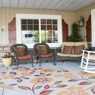 A cozy patio setup featuring wicker chairs, a cushioned swing bench, and a rocking chair on a decorative rug.