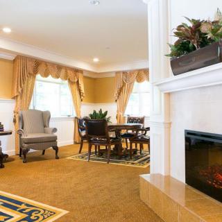 A cozy living room with a fireplace and adjacent dining area, featuring elegant armchairs and curtains.