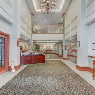 A spacious hotel lobby with a grand chandelier, featuring a reception desk and an upper balcony.