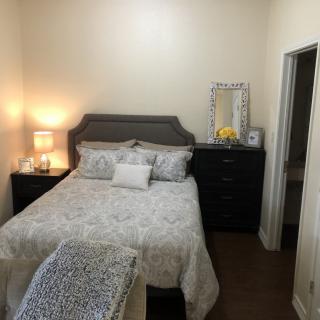 A cozy bedroom with a neatly made bed, bedside lamp, and dresser with a mirror.