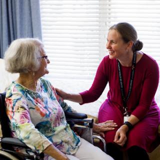 A caregiver engages in a warm conversation with an elderly woman in a cozy indoor setting.