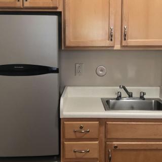 A small kitchen area with a refrigerator, sink, and wooden cabinets.