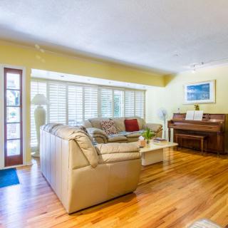 A cozy living room with a beige sofa, piano, and large windows allowing natural light.