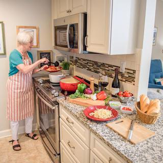 A woman in an apron prepares a meal in a home kitchen surrounded by various ingredients.