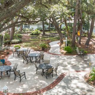 A tranquil outdoor patio area with tables and chairs surrounded by lush greenery and trees.