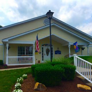 A yellow building with a ramp, flanked by American and blue flags, surrounded by well-maintained landscaping.