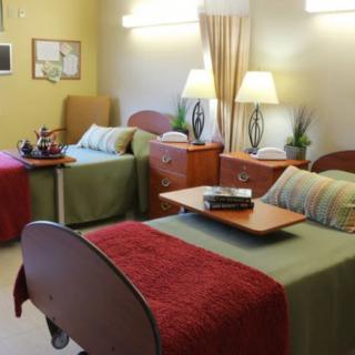 A hospital room with two neatly made beds, bedside tables, and soft lighting.