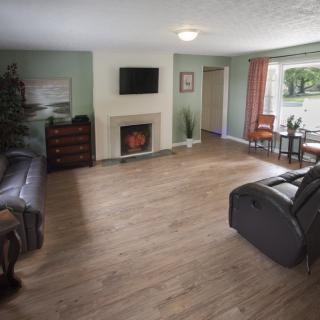 A spacious living room with hardwood flooring, featuring comfortable seating, a television mounted above a fireplace, and a cozy dining area by the window.