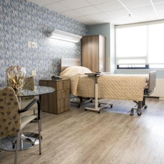 A well-lit and clean hospital patient room featuring a bed, chair, and modern furnishings.