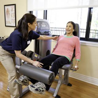A trainer assists a patient with exercises on an exercise machine during a physical therapy session.