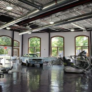 A spacious workshop featuring classic automobiles and fitness equipment, characterized by large windows and a modern industrial design.