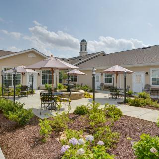 A sunny outdoor patio area with seating and umbrellas surrounded by lush landscaping.