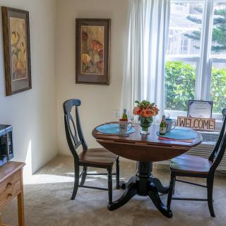 A cozy dining area with a round table and two chairs, bathed in natural light from a large window.