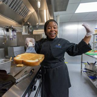 A cheerful chef in a kitchen holding a freshly toasted slice of bread.
