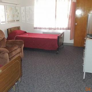 A simple bedroom with a single bed, chair, and dresser.