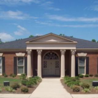 A classical-style brick building with columns and a neatly landscaped front yard.