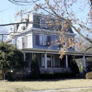 A large residential house with a porch, surrounded by bare trees in winter.
