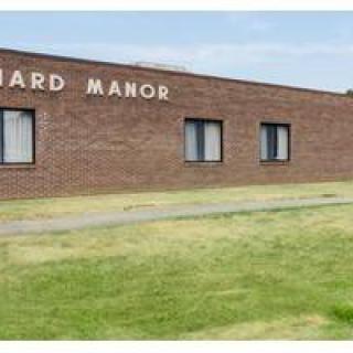 A brick building named 'Manor' with windows and a grassy front yard.