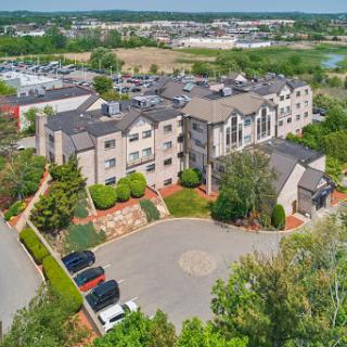 Aerial view of a residential building surrounded by greenery and a parking lot.