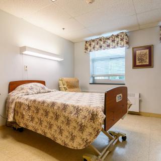 A clean and well-lit hospital room with a single bed and chair.