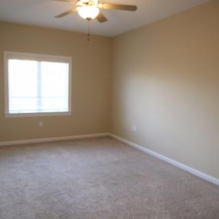 An empty room with beige walls, a carpeted floor, a window, and a ceiling fan.