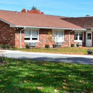 A charming single-story brick house surrounded by a well-kept lawn and autumn foliage.