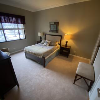 A cozy bedroom featuring a bed with a headboard, a lamp on the nightstand, and a window allowing natural light.