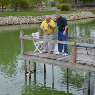 Two people fishing from a dock by a lake.