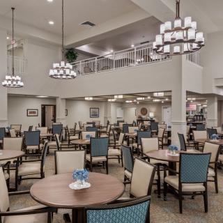 A spacious dining area with multiple tables and chairs, illuminated by elegant chandeliers.