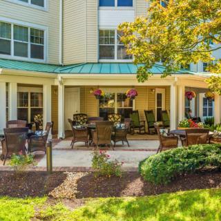 A cozy patio area with outdoor furniture outside a residential building, surrounded by lush greenery.