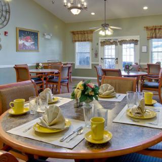 A dining room with tables set for a meal, featuring yellow crockery and neatly arranged napkins.