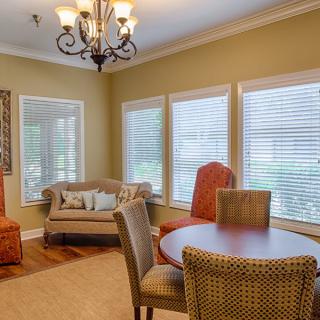 A cozy living and dining area featuring a round dining table, cushioned chairs, a loveseat, and large windows with blinds.