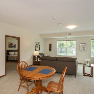 A cozy living space featuring a dining area with a wooden table and chairs, adjacent to a seating area with a sofa and large windows.