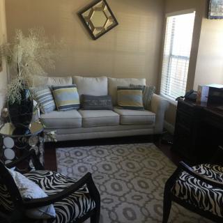 A cozy living room featuring a sofa with cushions, patterned chairs, a decorative rug, and wall art.