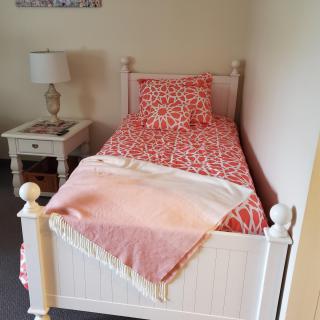 A cozy bedroom corner with a single bed adorned in pink patterned bedding and a bedside table with a lamp.