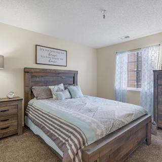 A cozy bedroom with a large bed, wooden furniture, and a window with sheer curtains.
