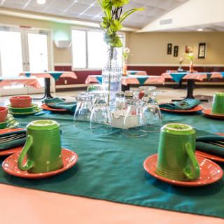A beautifully arranged dining table ready for an event, featuring colorful tableware and a floral centerpiece.
