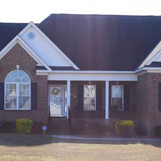 A brick exterior house with a porch and multiple windows.