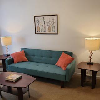 A cozy living room featuring a teal sofa with orange cushions, paired with stylish lamps and elegant artwork.