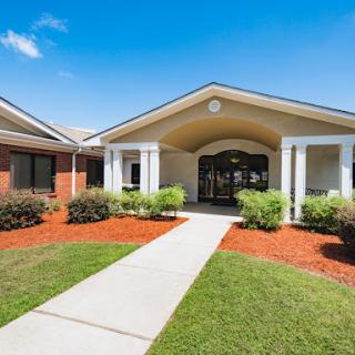 A welcoming entrance to a well-maintained building, surrounded by lush greenery and a clear blue sky.